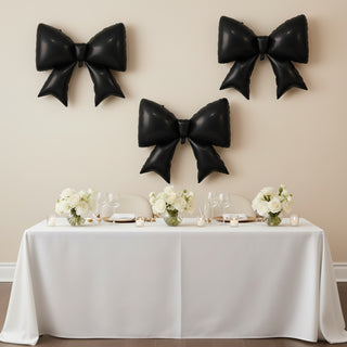 Black balloon bows above a decorated dining table with white floral centerpieces.