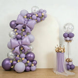 Purple balloon arch with bows and floral accents for events.