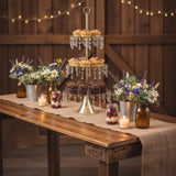 Dessert table with cupcakes, flowers, and candles in a rustic setting.
