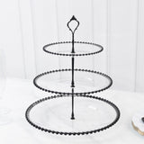Black three-tiered serving stand with beaded edges on a marble surface.