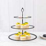 Three-tiered black cupcake stand with decorated cupcakes on a marble surface.