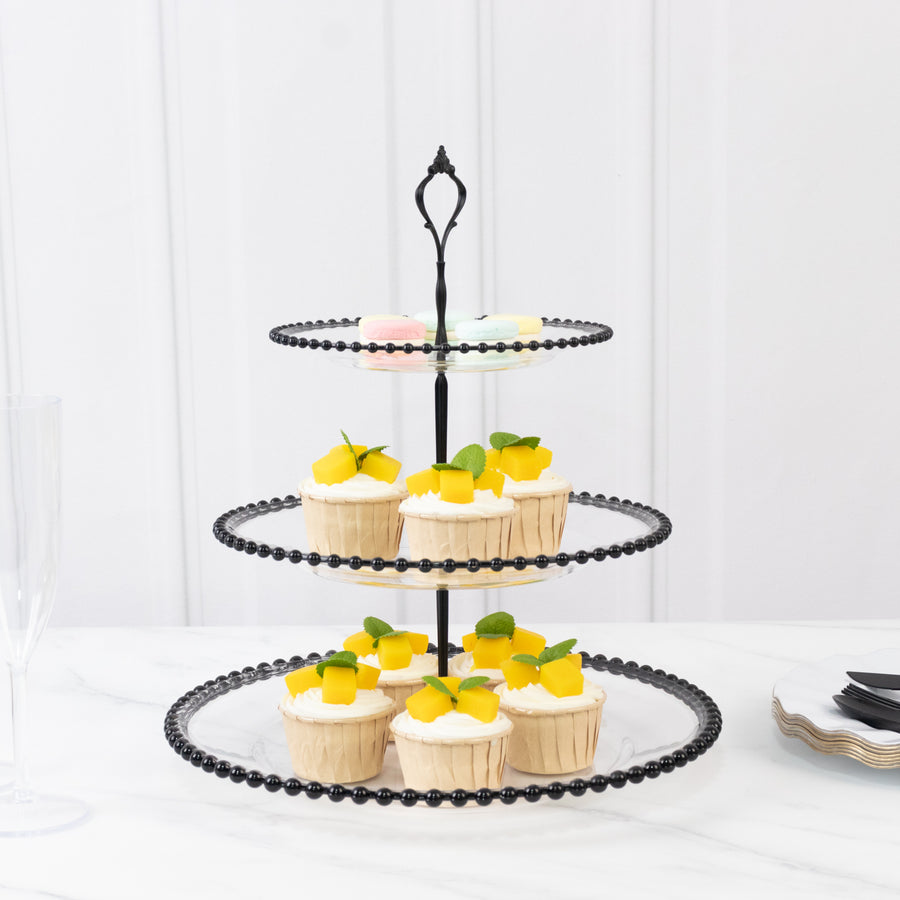 Three-tiered black cupcake stand with decorated cupcakes on a marble surface.