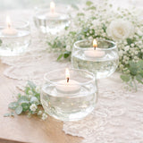 Floating candles in glass bowls with greenery and flowers on a table.