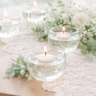 Floating candles in glass bowls with greenery and flowers on a table.