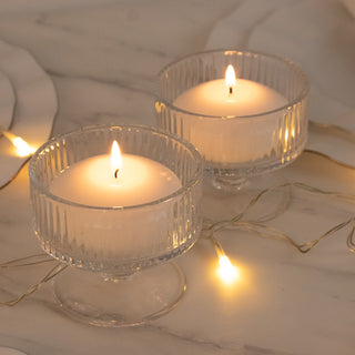 Two lit candles in clear glass holders with warm fairy lights on marble surface