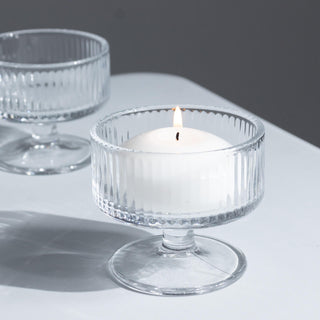 Lit white candle in a glass pedestal holder on a minimalist table