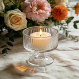 Lit candle in a glass pedestal holder with floral arrangement background