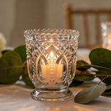 Lit glass candle holder with warm candlelight and green eucalyptus leaves