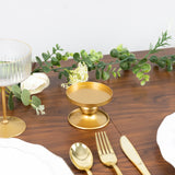 Gold dessert stand on a wooden table with floral arrangement and tableware.