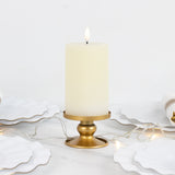 Elegant cream pillar candle in a gold holder on a table with white plates and string lights.