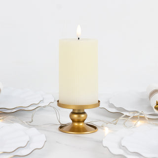 Elegant cream pillar candle in a gold holder on a table with white plates and string lights.