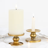White pillar candle and tapered candle on gold holders with string lights