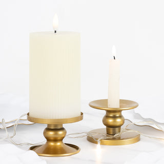 White pillar candle and tapered candle on gold holders with string lights