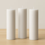 Set of three white pillar candles on a wooden surface.