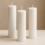 White pillar candles in varying heights against a soft beige background.