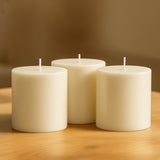 Three ivory pillar candles on a wooden table.