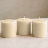 Set of three cream-colored pillar candles on a plain background.