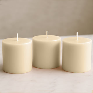 Set of three cream-colored pillar candles on a plain background.