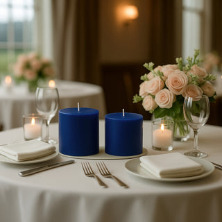 Blue pillar candles on a beautifully set dining table with flowers and glassware.