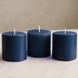 Three navy blue pillar candles on a marble countertop.
