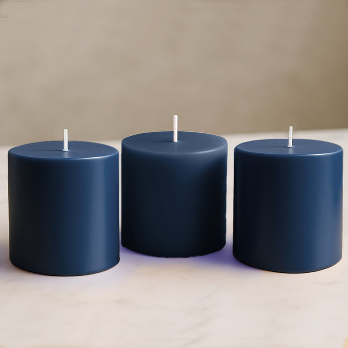 Three navy blue pillar candles on a marble countertop.