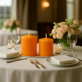Orange candles on a dining table with flowers and glassware in a restaurant setting.