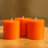Three vibrant orange candles on a wooden table.