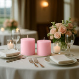 Pink candles on a beautifully set dining table with flowers and glassware.