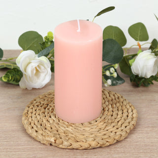 Pink pillar candle on a woven coaster with greenery and flowers.