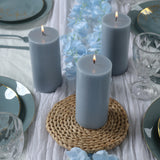 Gray pillar candles on a table setting with blue rose decorations and elegant dinnerware.