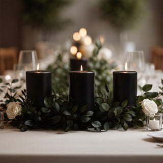 Elegant black candles surrounded by greenery and white roses on a dining table.