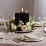 Elegant black candles surrounded by soft pink and white flowers on a dining table.