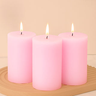 Three pink candles with flames on a wooden tray.