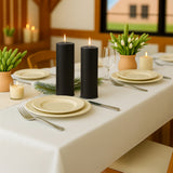 Black pillar candles on a beautifully set dining table with greenery and dinnerware.