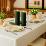 Green candles on a beautifully set dining table with elegant tableware and greenery.