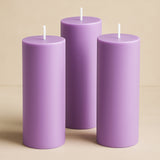 Three purple pillar candles of varying heights against a neutral background.