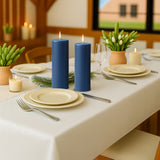 Blue candles on a beautifully set dining table with plates and greenery.