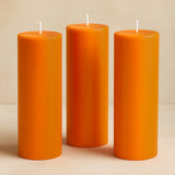 Set of three vibrant orange pillar candles in varying heights.