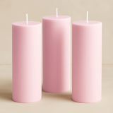 Three pink pillar candles in varying heights on a neutral background.