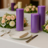 Purple candles with floral arrangement on a dining table setting.