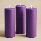 Purple pillar candles in varying heights on a neutral background.
