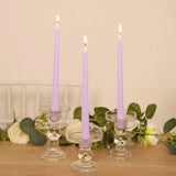 Three lavender taper candles in clear glass holders, elegantly lit.