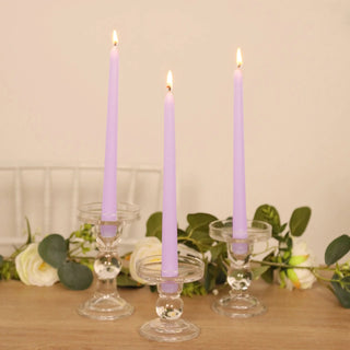Three lavender taper candles in clear glass holders, elegantly lit.