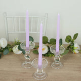 Purple taper candles in clear glass holders on a wooden table with floral accents.