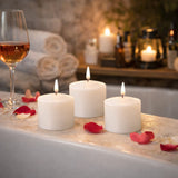 Three white candles with lit wicks surrounded by rose petals in a cozy bath setting.
