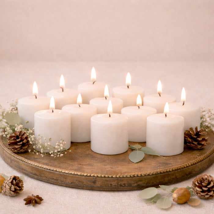 White pillar candles arranged on a decorative tray with greenery and pinecones.