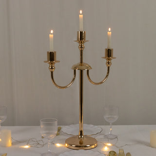 Elegant three-arm gold candle holder with lit candles on a table.