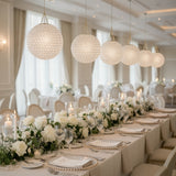 Elegant dining setup with floral arrangements and hanging lights in a banquet hall.