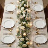 Elegant dining table set with white plates, gold utensils, and floral centerpiece.