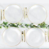 Elegant white plates with gold rims arranged with greenery and cutlery.